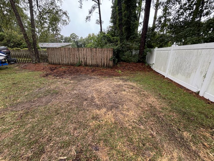 Cleared backyard between a wooden fence and a white vinyl fence after a pine removal and stump grinding in Myrtle Beach, SC