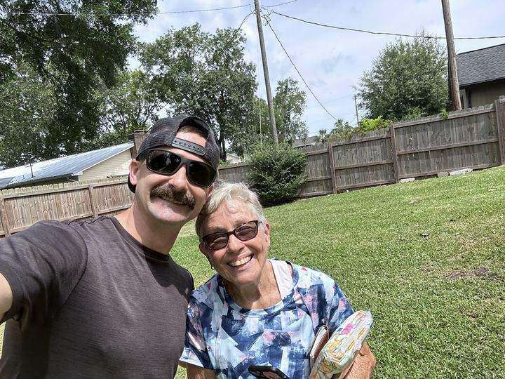 Corey smiling beside a happy older customer in her backyard after a tree job