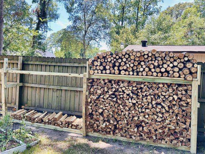 Firewood rack stacked full of split oak in a fenced backyard