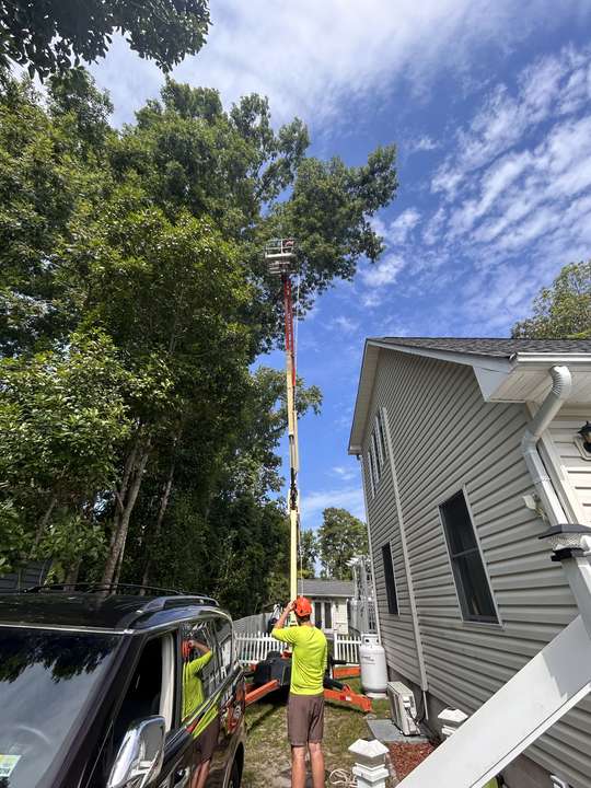 Tracked lift extended high beside a two-story house with crew in hi-vis below in Myrtle Beach, SC