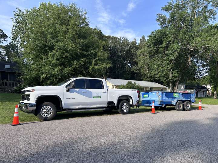 White pickup and dump trailer parked at a residential jobsite under tall trees in Myrtle Beach, SC